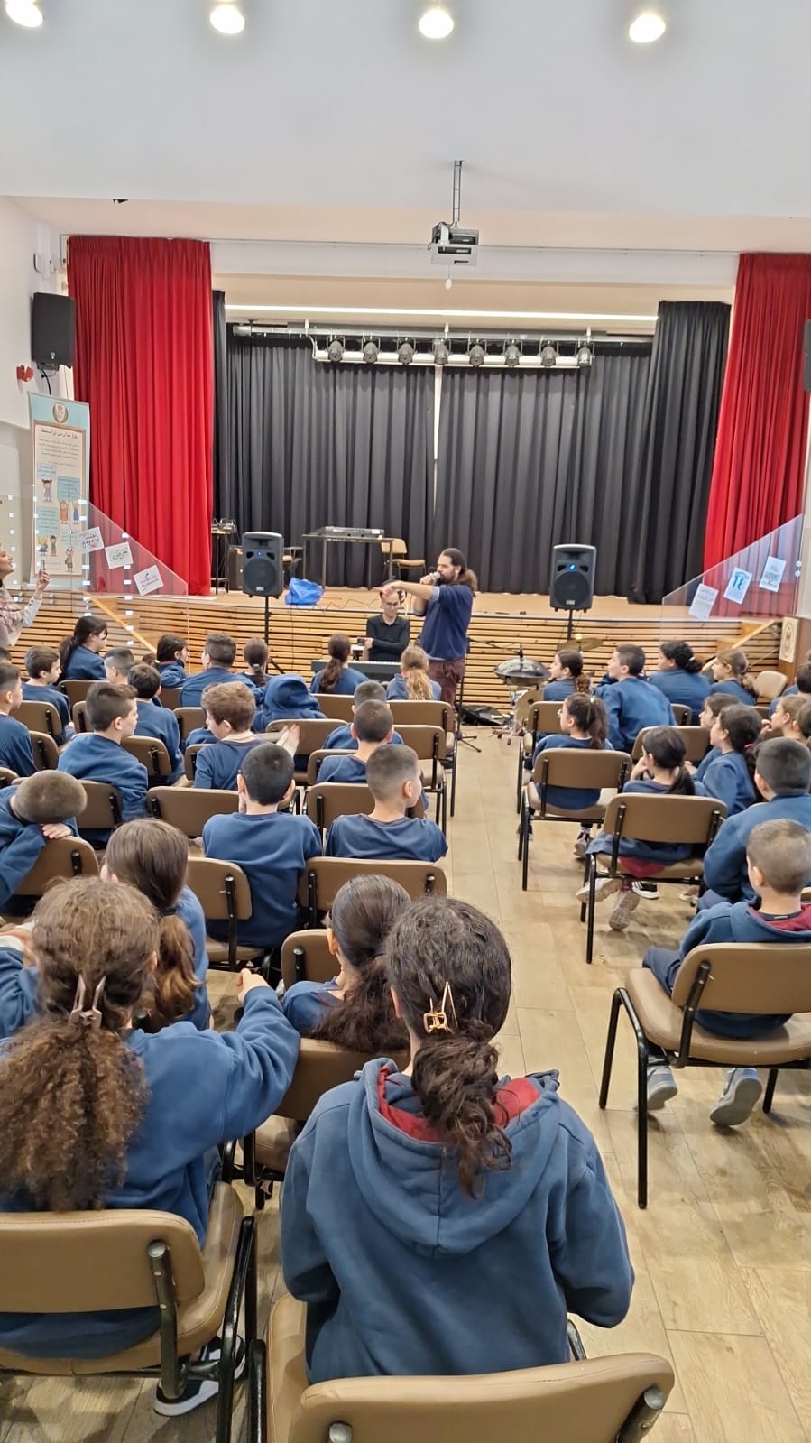 A school hall full of pupils seen from behind during an event.