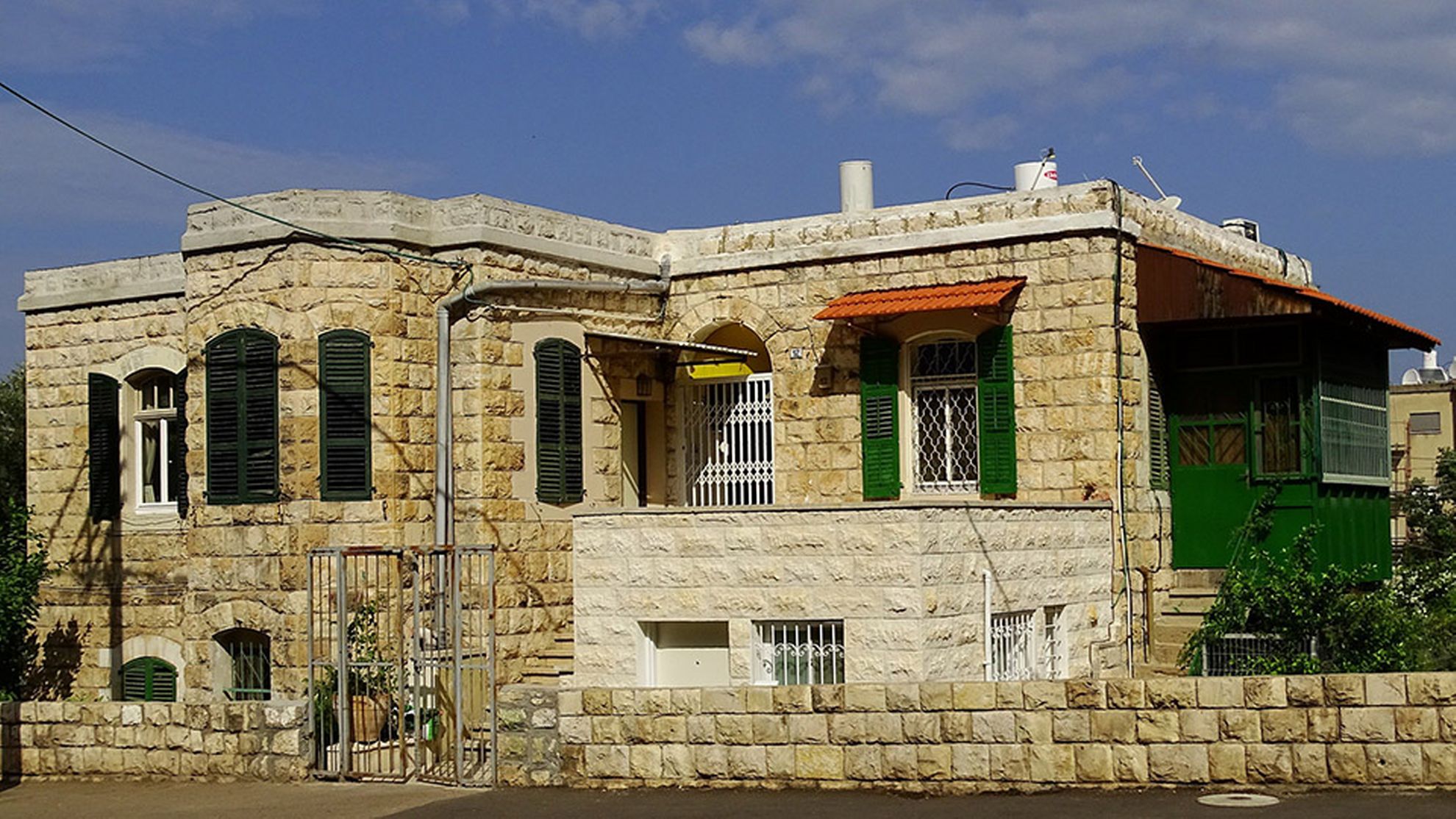 A stone heritage house in Haifa with green shutters.